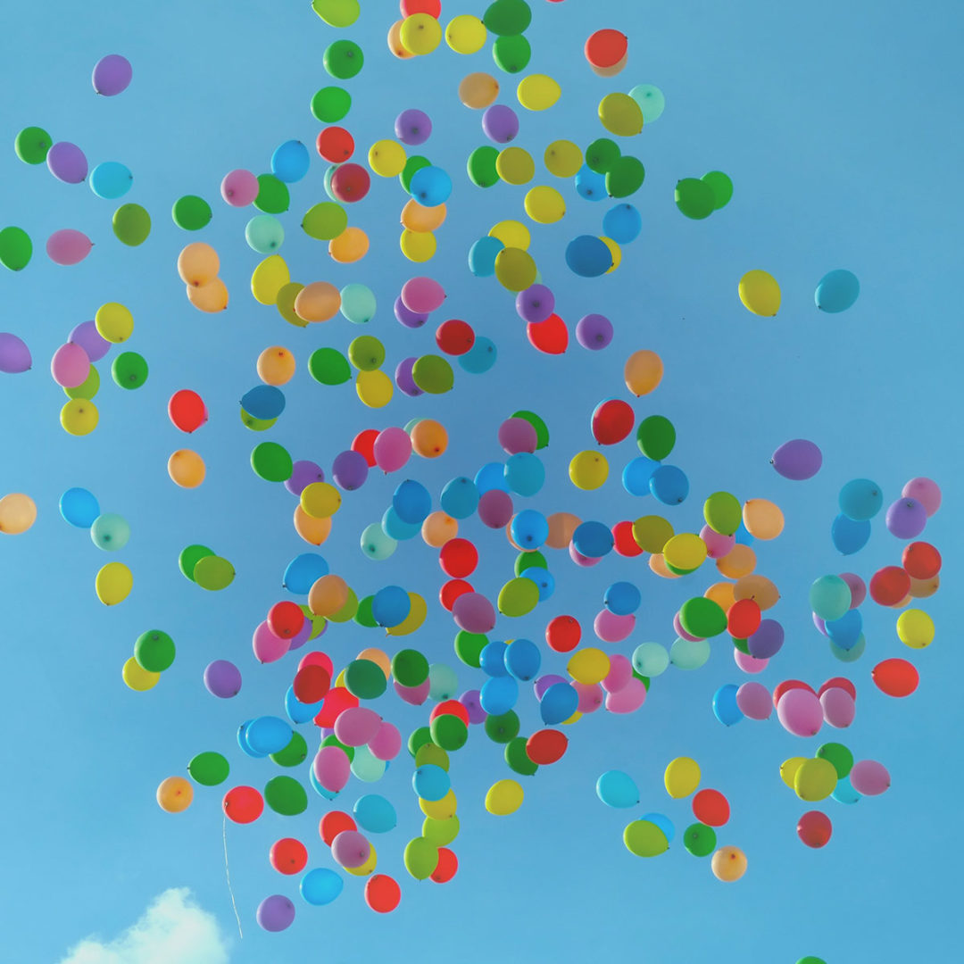 Colorful balloons floating across a pale blue sky.