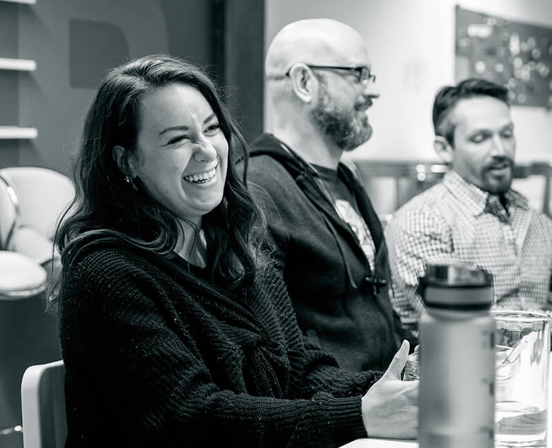 Three idfive team members sit in a row at a table, enjoying a moment of laughter.