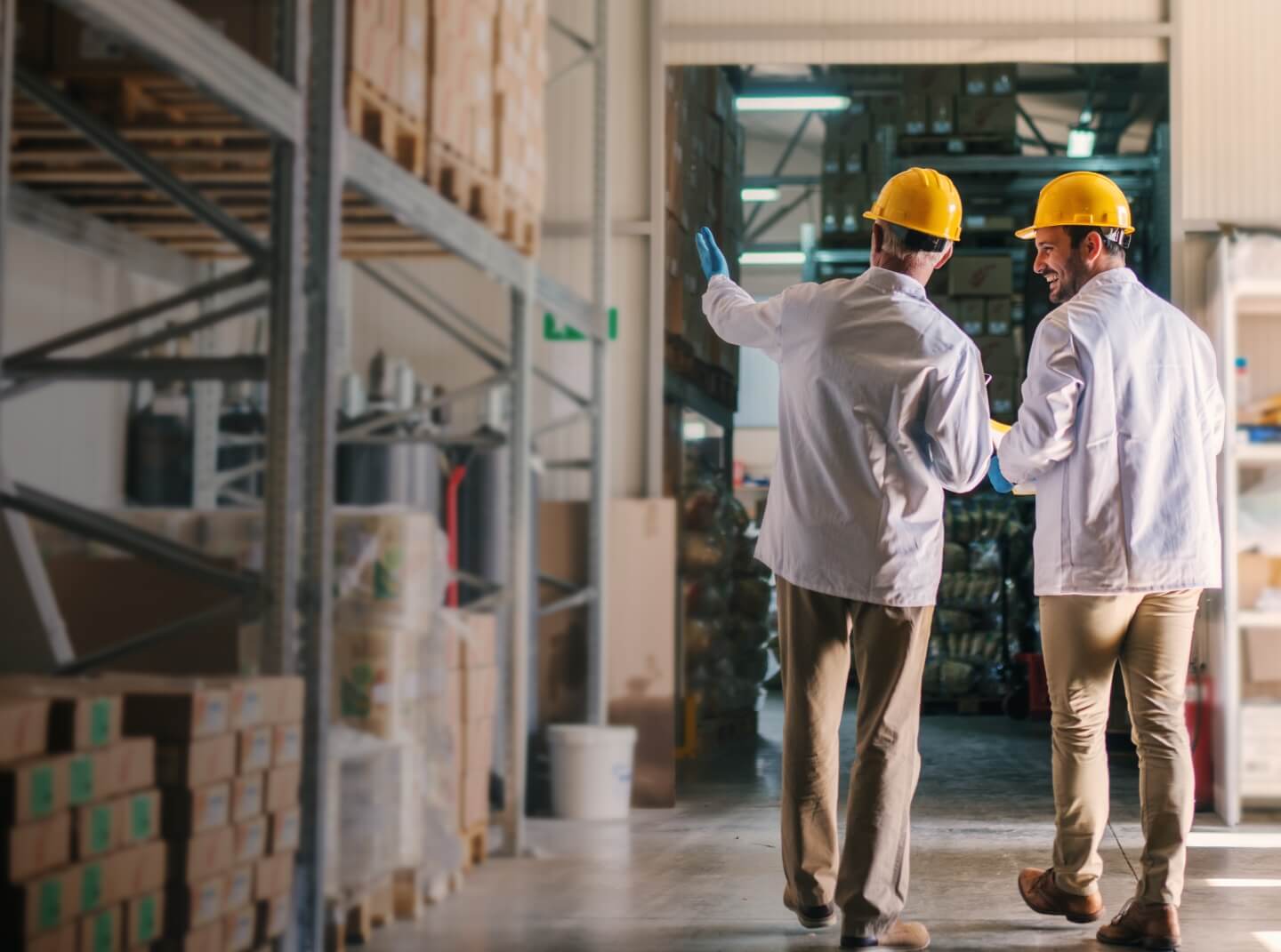 Two men wearing hard hats stand in a warehouse