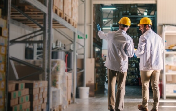 Two men wearing hard hats stand in a warehouse
