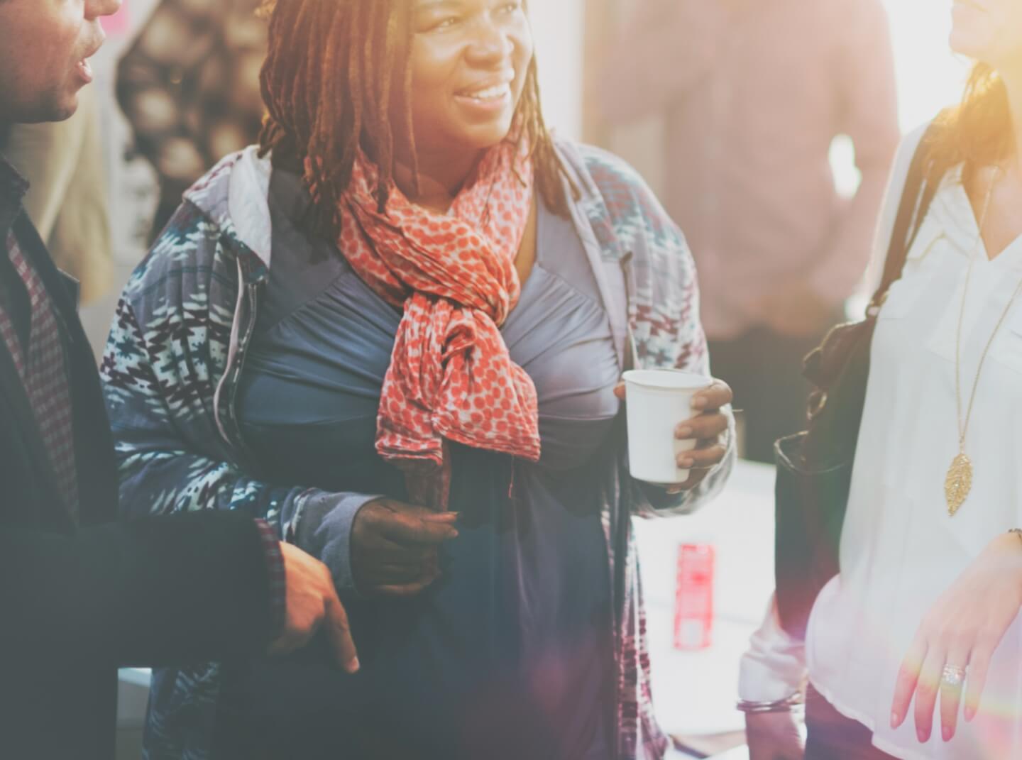 A woman in a scarf smiles while chatting with colleagues at a networking event