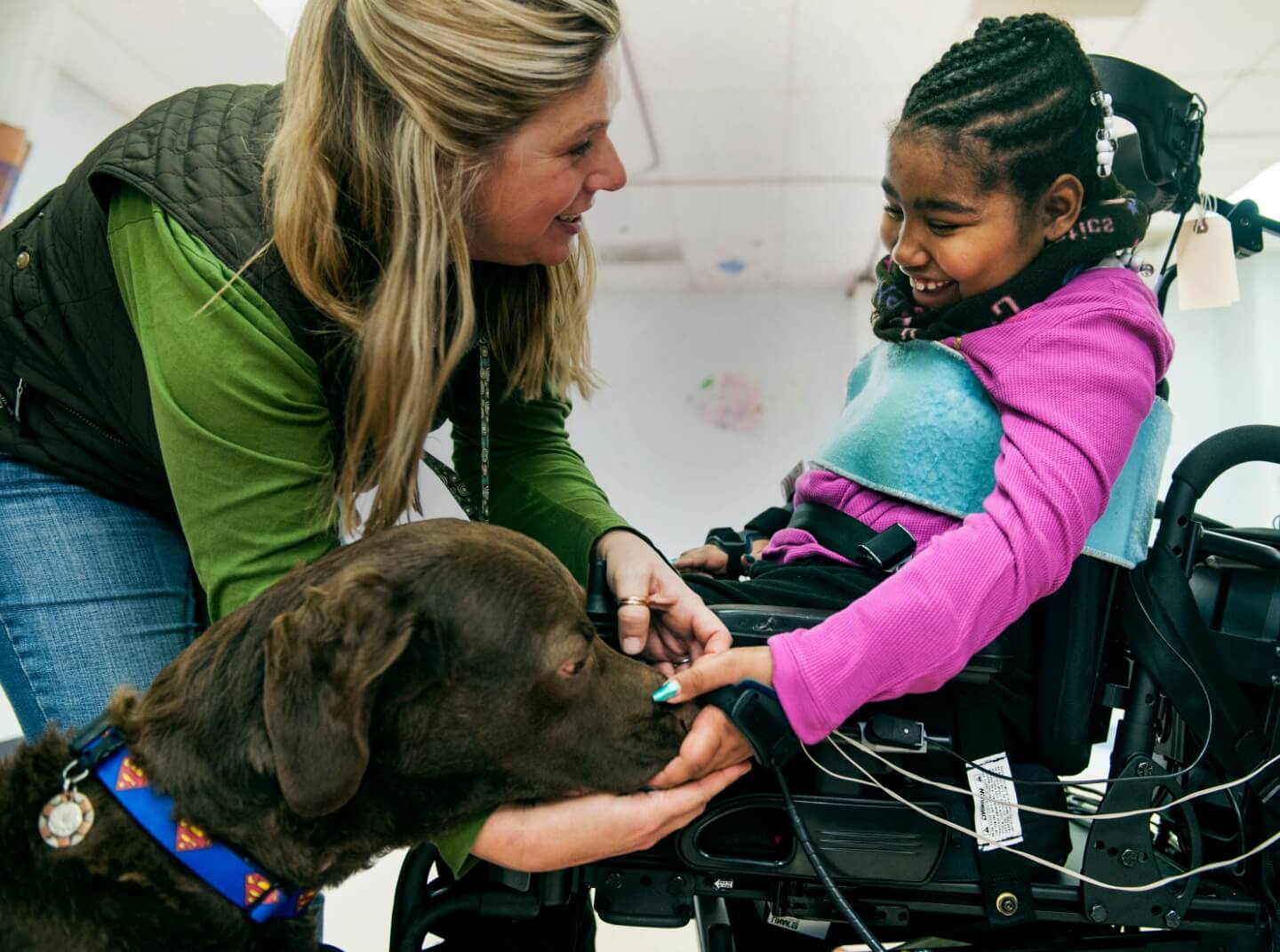 A caretaker introduces a service dog to a young girl in a mechanized wheelchair