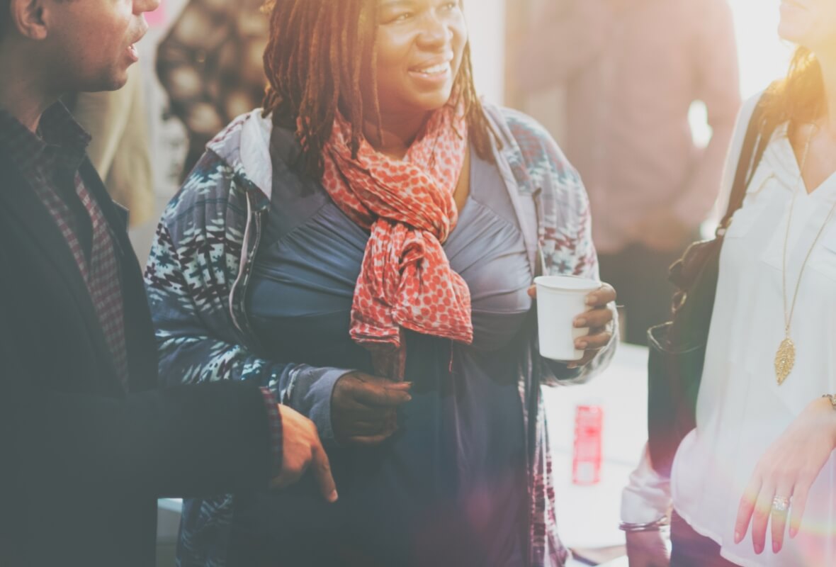 A woman in a scarf smiles while chatting with colleagues at a networking event