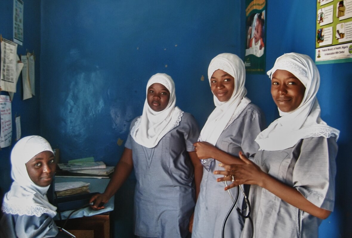 Four nurses smile while standing in the vestibule of an African health care facility