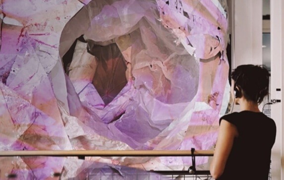 An art patron wearing headphones looks out over a railing at an art installation, a mixed media tunnel sculpture