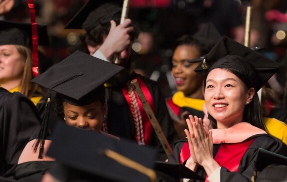 A University of Maryland graduate in academic regalia applauds during a commencement ceremony