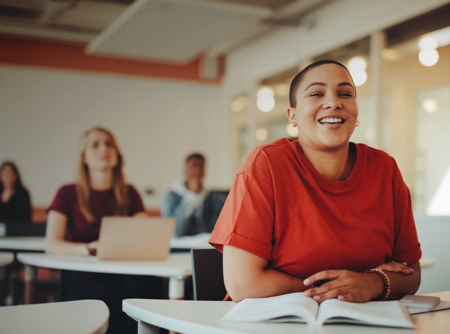 A young adult student smiles in a classroom, with classmates in the background