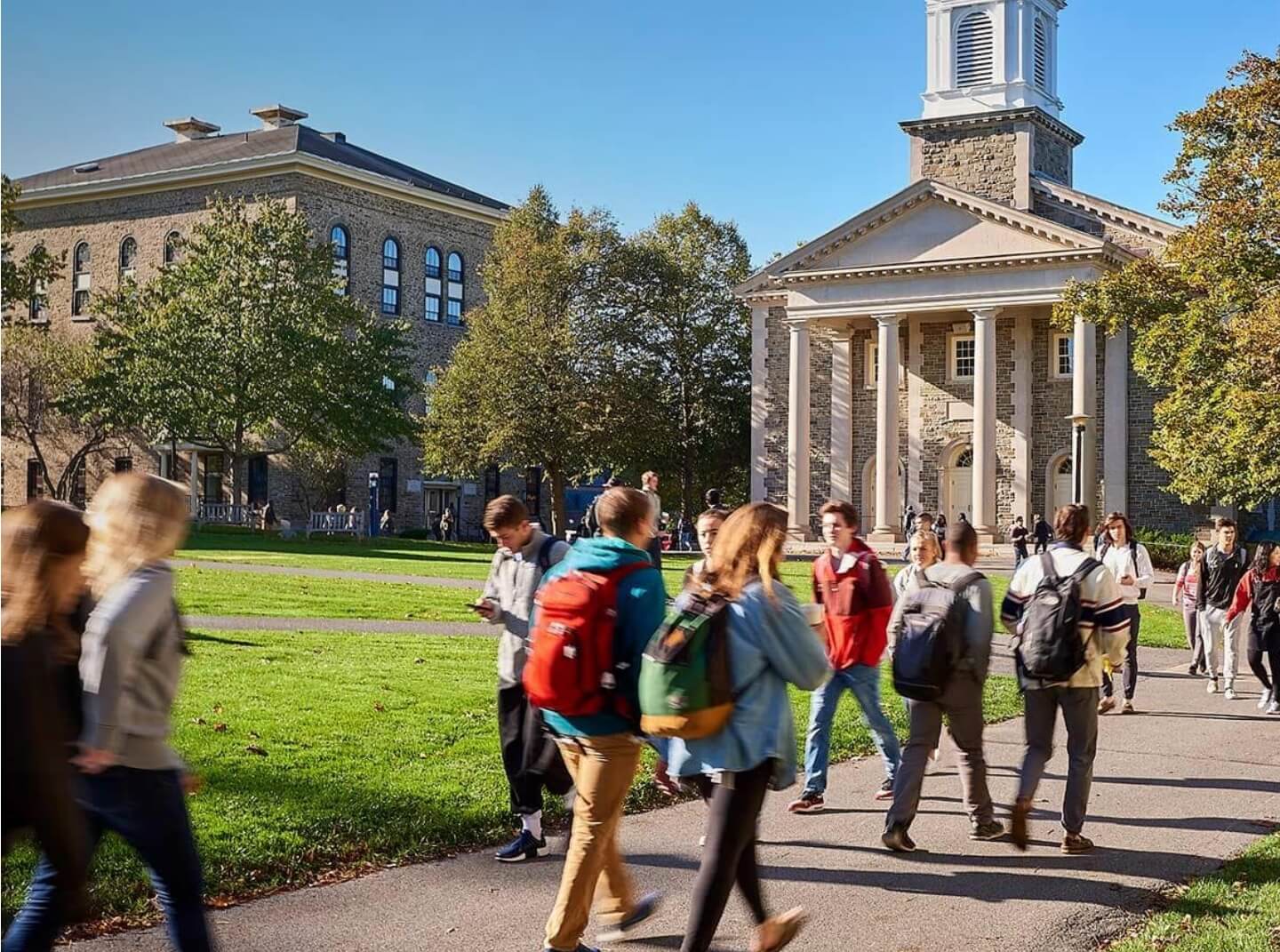 Colgate students hurry to their classes on a sunny day in early fall, the chapel visible in the background