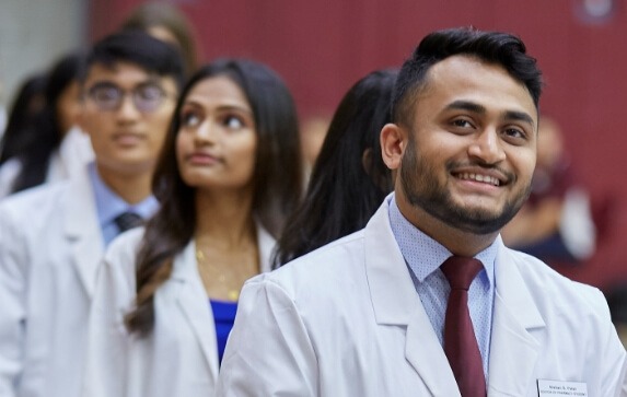 USciences Online graduates in lab coats line up to receive their degrees at commencement