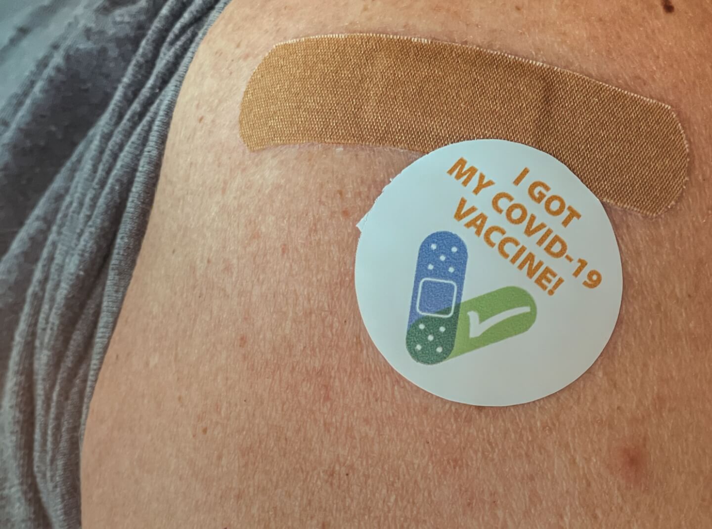 A woman's arm with a band-aid and sticker that reads "I got my COVID-19 vaccine"