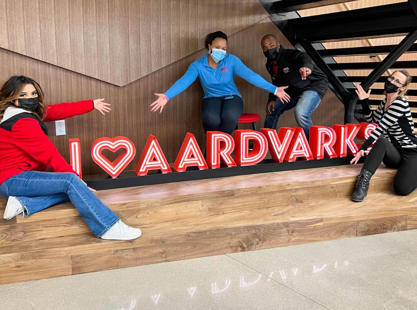 Masked Aims Community College students pose around a neon sign in a campus common area, the sign reads "I heart aardvarks"
