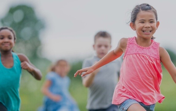 A young girl smiles while being chased by two other children in a game of tag
