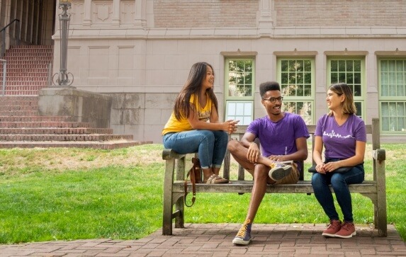 Three U-Dub students sit on a bench on campus