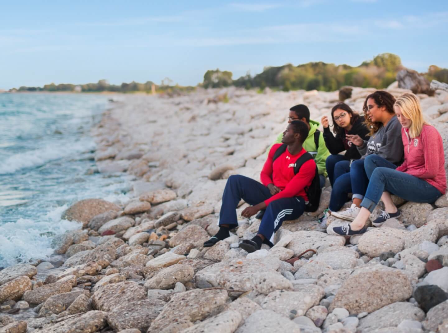 A group of Carthage College students sits on rocks, looking out over Lake Michigan.