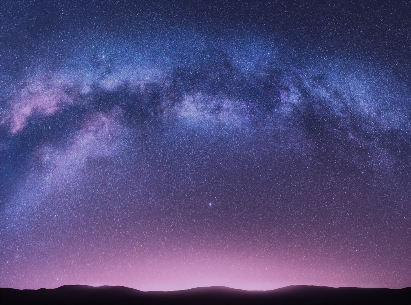 Nighttime photo of the Milky Way visible over a mountainous horizon