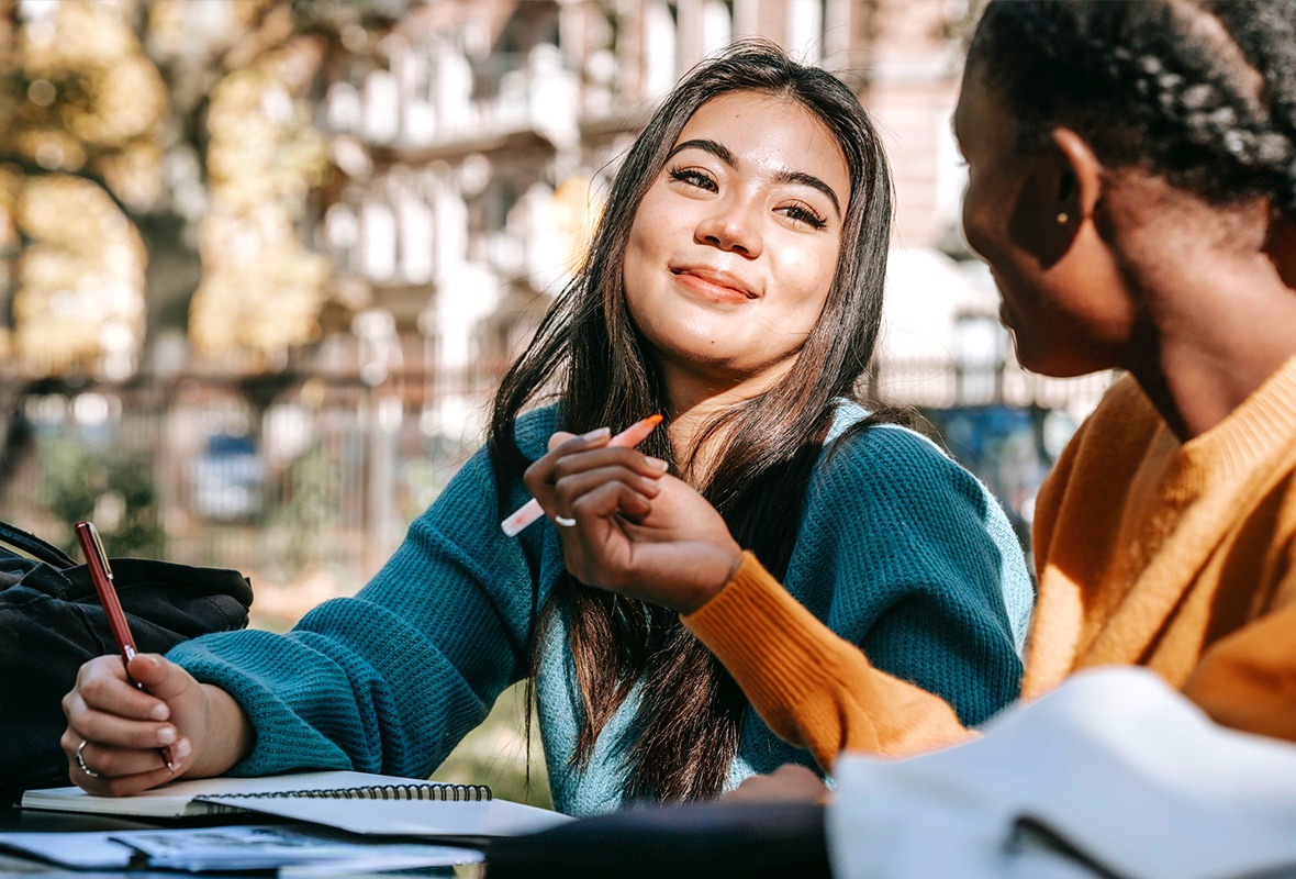 Two young female students working together on school work outside.
